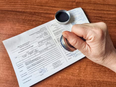 Kirov, Russia - March 18, 2024: Close-up of hand pressing a seal onto paper. Woman Applying Seal to Official Document on Table