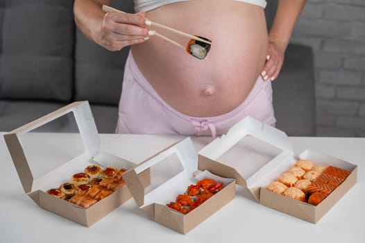 A pregnant woman stands at a table with rolls. Close-up of the belly