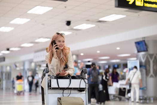 Young woman traveler with pink hair using phone in airport terminal.