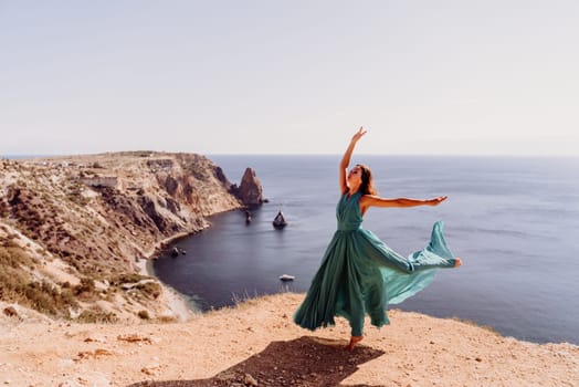 Woman green dress sea. Female dancer posing on a rocky outcrop high above the sea. Girl on the nature on blue sky background. Fashion photo