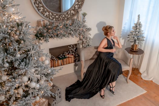 Portrait of a wealthy mature woman with evening make-up and hairstyle posing in a black dress on the background of the Christmas room. Luxurious lifestyle. Christmas holidays concept.