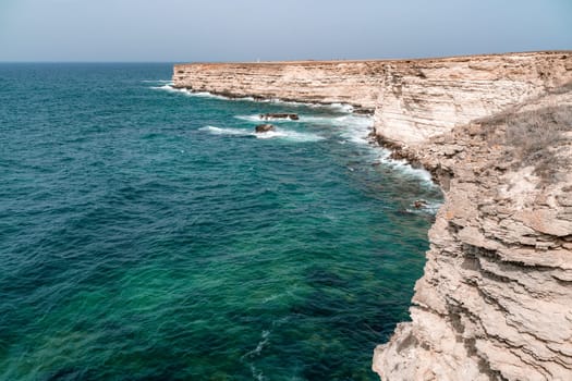 The ocean is calm and the shoreline is rocky. The water is a deep blue color. The rocks are jagged and the waves are small. The scene is peaceful and serene