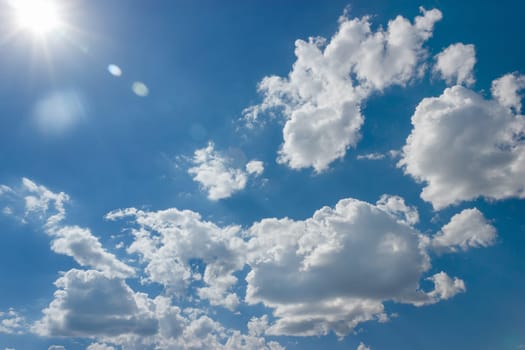 Serene natural landscape with a vivid electric blue sky, fluffy white cumulus clouds, and the sun shining through, creating a calm and peaceful atmosphere.