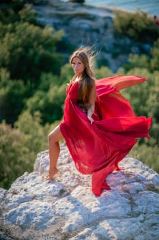 Woman sunset sea red dress, back view a happy beautiful sensual woman in a red long dress posing on a rock high above the sea on sunset