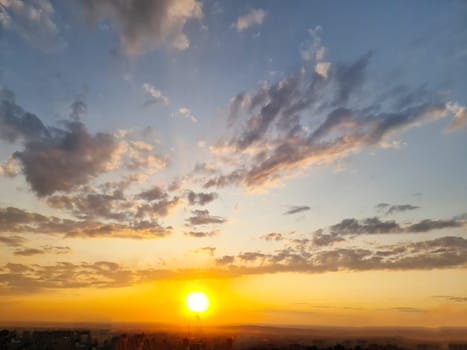 The sun sets behind the city, setting behind the horizon, picturesquely illuminating the various clouds with delicate colors.