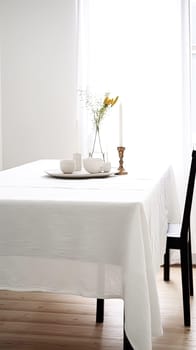 A table with a white tablecloth and a vase of flowers in the center. The table is set with plates, cups, and utensils. Scene is elegant and inviting