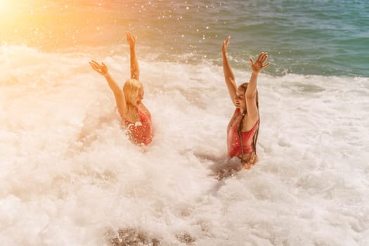 Women ocean play. Seaside, beach daytime, enjoying beach fun. Two women in red swimsuits enjoying themselves in the ocean waves and raising their hands up