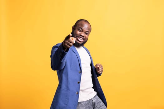 Portrait of flashy motivational speaker pointing finger to audience with determination, isolated over studio background. Expressive vigorous BIPOC lecturer showing intense emotion