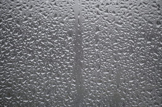 Close-up view of a glass surface covered with many water droplets of various sizes, creating a textured pattern