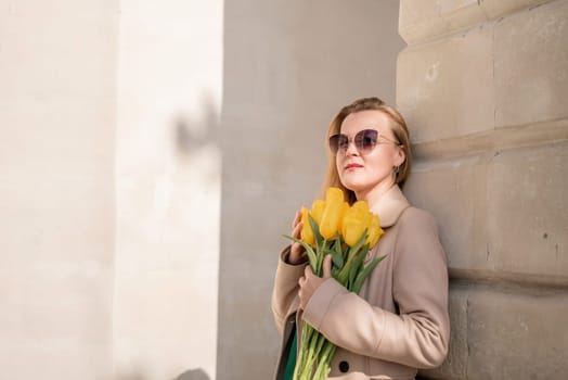 Woman holding yellow tulips, leaning against stone wall. Women's holiday concept, giving flowers