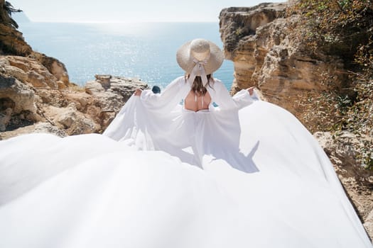 A woman in a white dress is standing on a rocky beach with her hat on. The scene is serene and peaceful, with the woman enjoying the view of the water.