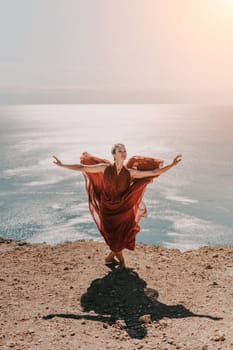 Woman red dress sea. Female dancer in a long red dress posing on a beach with rocks on sunny day. Girl on the nature on blue sky background