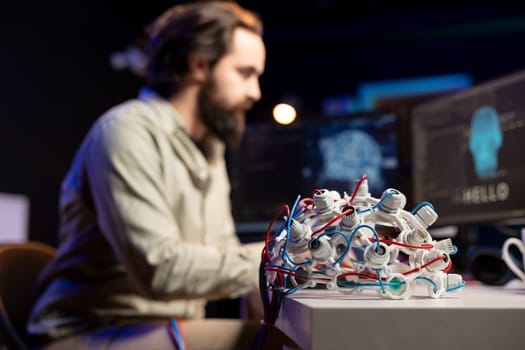 Focus on EEG headset used by engineer in blurry background to upload consciousness into computer. Close up shot of high tech gear used by IT expert to create connection between brain and PC