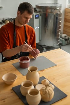 Potter paints ceramic dishes with a brush. Vertical photo