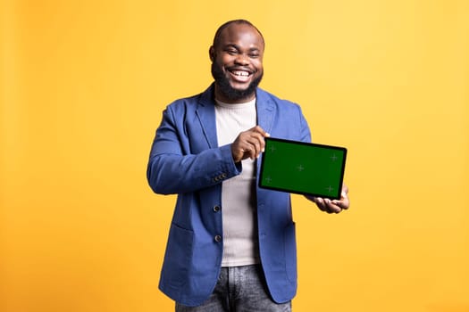 Happy african american laughing while man holding green screen tablet, doing recommendation. Overjoyed BIPOC person presenting chroma key device, isolated over studio background