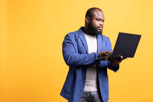 Man looking at business diagram and figures on laptop, isolated over studio background. BIPOC employee checking company financial annual report charts on notebook screen