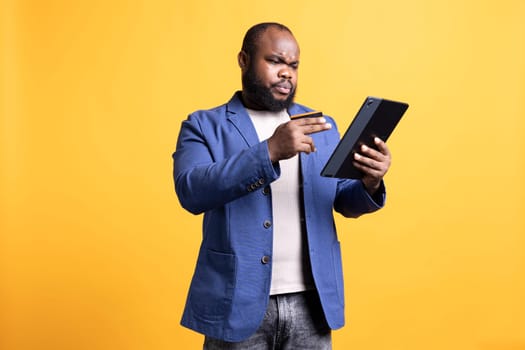 Man with frown on face while adding payment method on website, seeing insufficient funds error, studio background. Upset person getting transaction rejected, wrongly typing credit card data on tablet