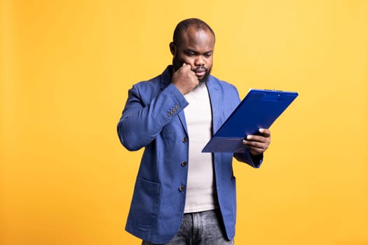 African american man browsing though financial report pages, isolated over studio background. Worker reading clipboard with files containing economic graphs and figures, solving business tasks