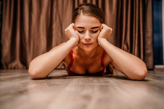 Young woman in red corset and black leather pants. Sexy seductive brunette, fitness instructor doing stretching and pilates on yoga mat at home. Female fitness yoga concept. Role play. Entertainment