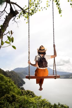 Young female tourist enjoying landscape sitting on a swing in Bali, Indonesia. Vertical image. Vacation concept.