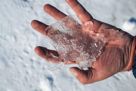 man's hand holds a piece of ice in winter close-up