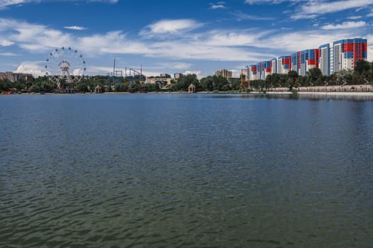 SHYMKENT, KAZAKHSTAN - JULY 07, 2023: View of the Altyn Eye Park and Ferris wheel from the lake in Shymkent in summer