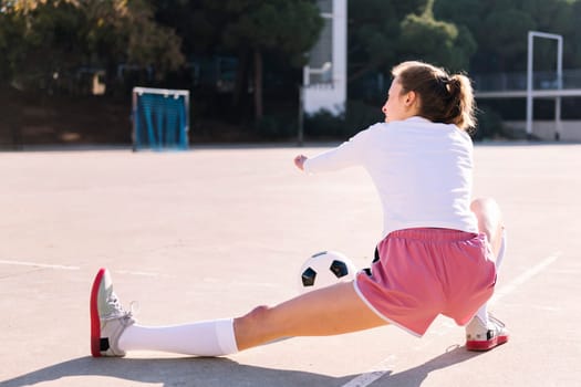 rear view of a young caucasian woman with a soccer ball stretching legs in a urban football court, concept of sport and active lifestyle, copy space for text