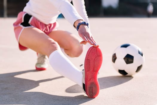unrecognizable woman with a soccer ball stretching legs in a football court, concept of sport and active lifestyle