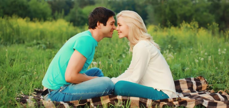 Portrait of beautiful happy smiling young couple in love lying together on the grass looking at each other having a picnic, summer park