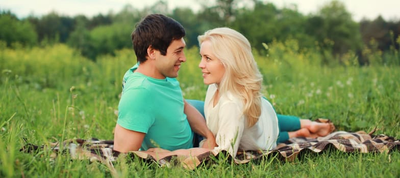 Portrait of beautiful happy smiling young couple in love lying together on the grass looking at each other having a picnic, summer park