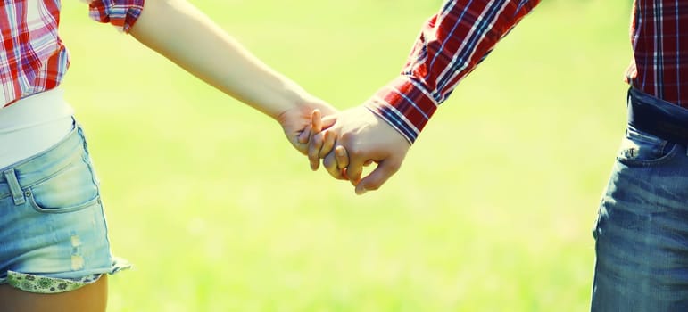 Close up of young couple holding hands, man and woman in love together in summer park