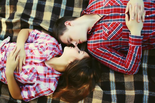 Portrait of happy caucasian young couple lying on the blanket together outdoors in summer park, top view