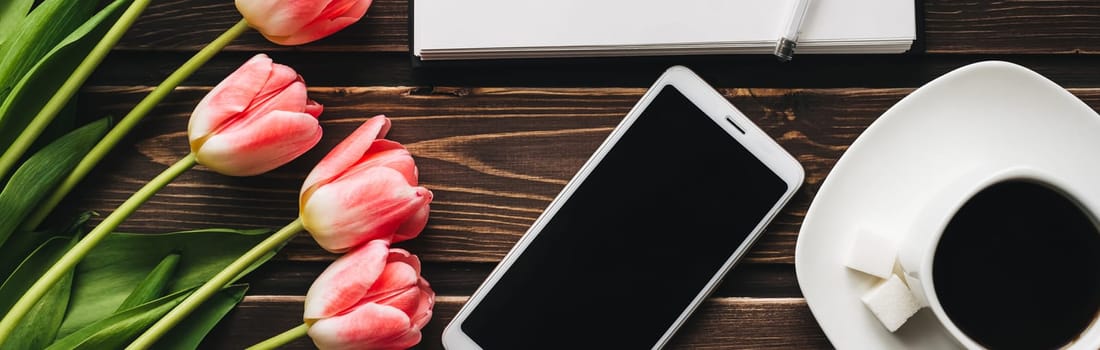 bouquet of pink tulips with a Cup of coffee and a smartphone on a wooden table. Blank Notepad template greeting cards. Flat lay, top view