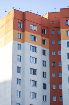 In the backdrop of a blue sky stands a towering building, showcasing urban design and composite material. The facade of the condominium reflects the azure sky in the cityscape