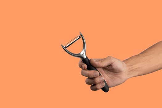 Black male hand holding a potato peeler isolated on orange background. High quality photo