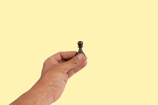 Isolated hand holding a chess figure on yellow background. High quality photo
