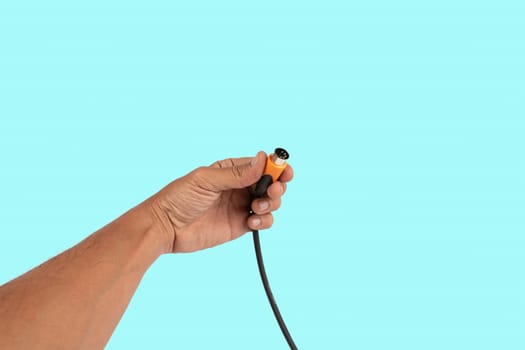 Black male hand holding a MIDI audio cable isolated light on cyan background. High quality photo