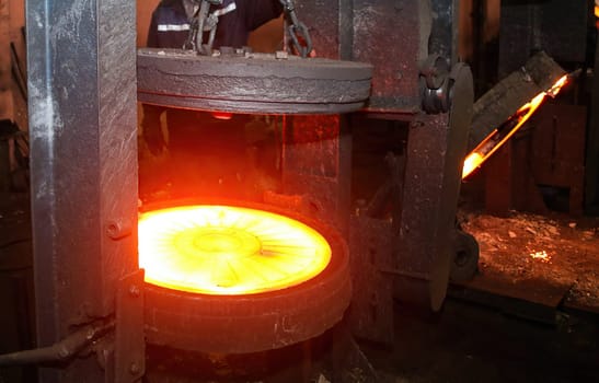 Industrial metalworking or manufacturing concept. Glowing hot round metal disc forging press isolated on black background. Industrial concept of power, energy, and strength.