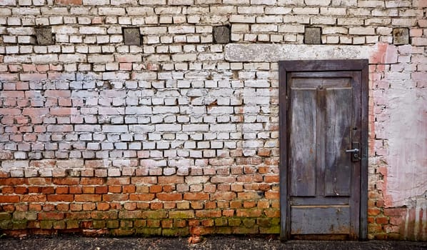 The vibrant blue wooden door, set against the weathered brick wall and adorned with remnants of whitewash, exudes a sense of history and charm, creating a timeless and welcoming atmosphere.