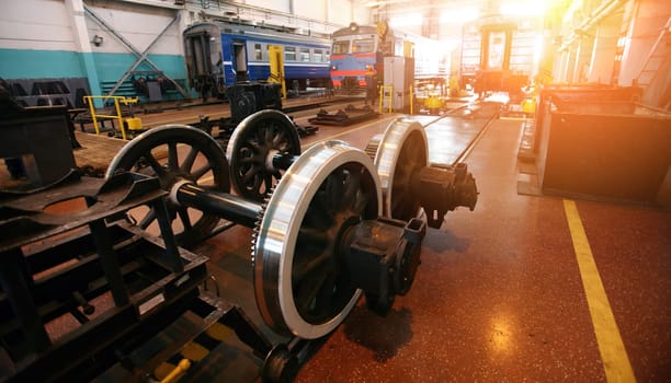 The workshop showcases the maintenance of railway equipment with a focus on a locomotive and a set of gleaming train wheels. Workers are possibly present, tending to the overhaul and repair of these vital components that keep the transportation network running smoothly. The setting suggests routine upkeep, keeping safety and efficiency at the forefront.