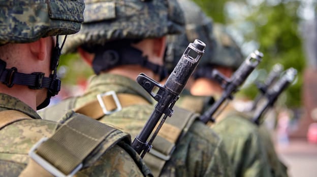 A soldier in full gear stands at attention with a rifle, wearing a helmet and camouflage uniform. Blurred background adds focus and determination to his readiness and vigilance.