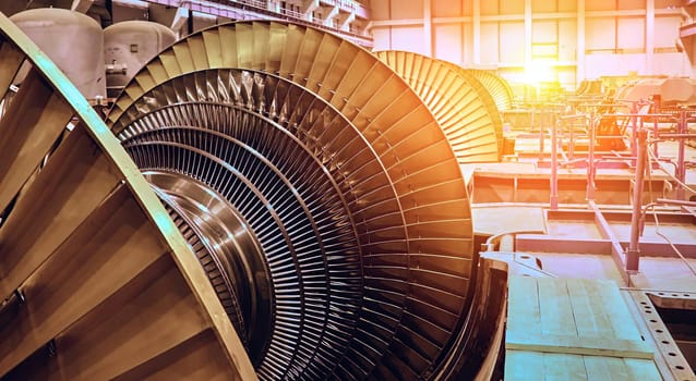 A close-up view of a large turbine blade inside a power plant, bathed in the warm light of the afternoon sun. The intricate design of the blades is highlighted, showcasing the complex engineering involved in generating power.