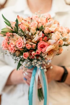 A woman is holding a bouquet of pink flowers with white accents. The bouquet is tied with a blue ribbon