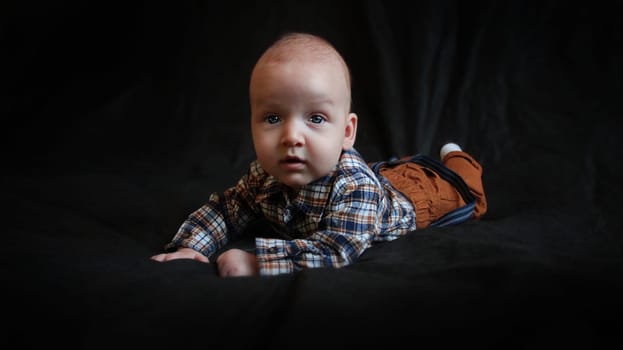 A kid in mustard pants and a plaid shirt lies on a black background. High quality photo