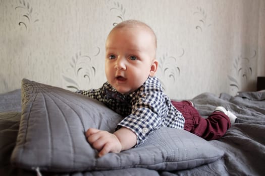 A baby in a plaid shirt and maroon pants lies on the bed. High quality photo