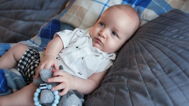 A baby in light clothes is lying on the bed. He is lying in a blue plaid blanket on a gray bed. High quality photo