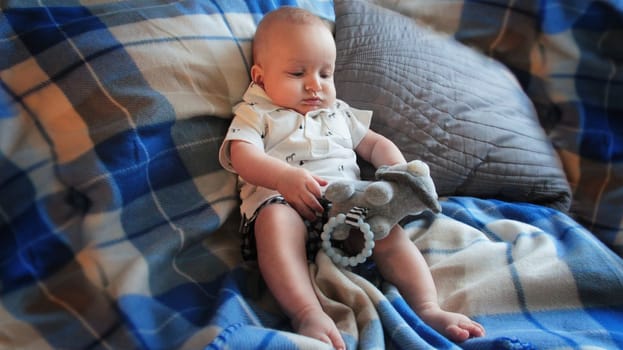 A baby in light clothes is lying on the bed. He is lying in a blue plaid blanket on a gray bed. High quality photo