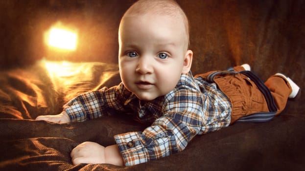 A kid in mustard pants and a plaid shirt lies on a black background. High quality photo