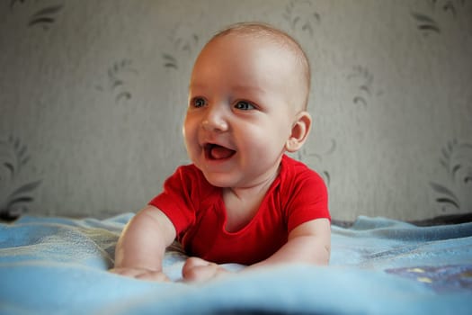 Baby in a red bodysuit lying on a blue blanket. High quality photo