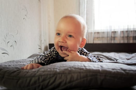 A baby in a plaid shirt and maroon pants lies on the bed. High quality photo